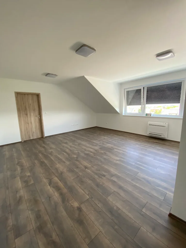 Tágas, világos helyiség és parketta padlóburkolat, rolós ablakok